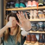 scarpiera di sfondo e in primo piano una donna che si mette le mani davanti agli occhi