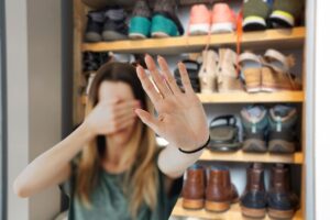 scarpiera di sfondo e in primo piano una donna che si mette le mani davanti agli occhi