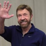 Chuck Norris con t-shirt blu saluta verso l'obiettivo.