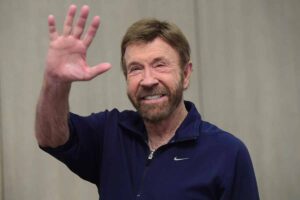 Chuck Norris con t-shirt blu saluta verso l'obiettivo.