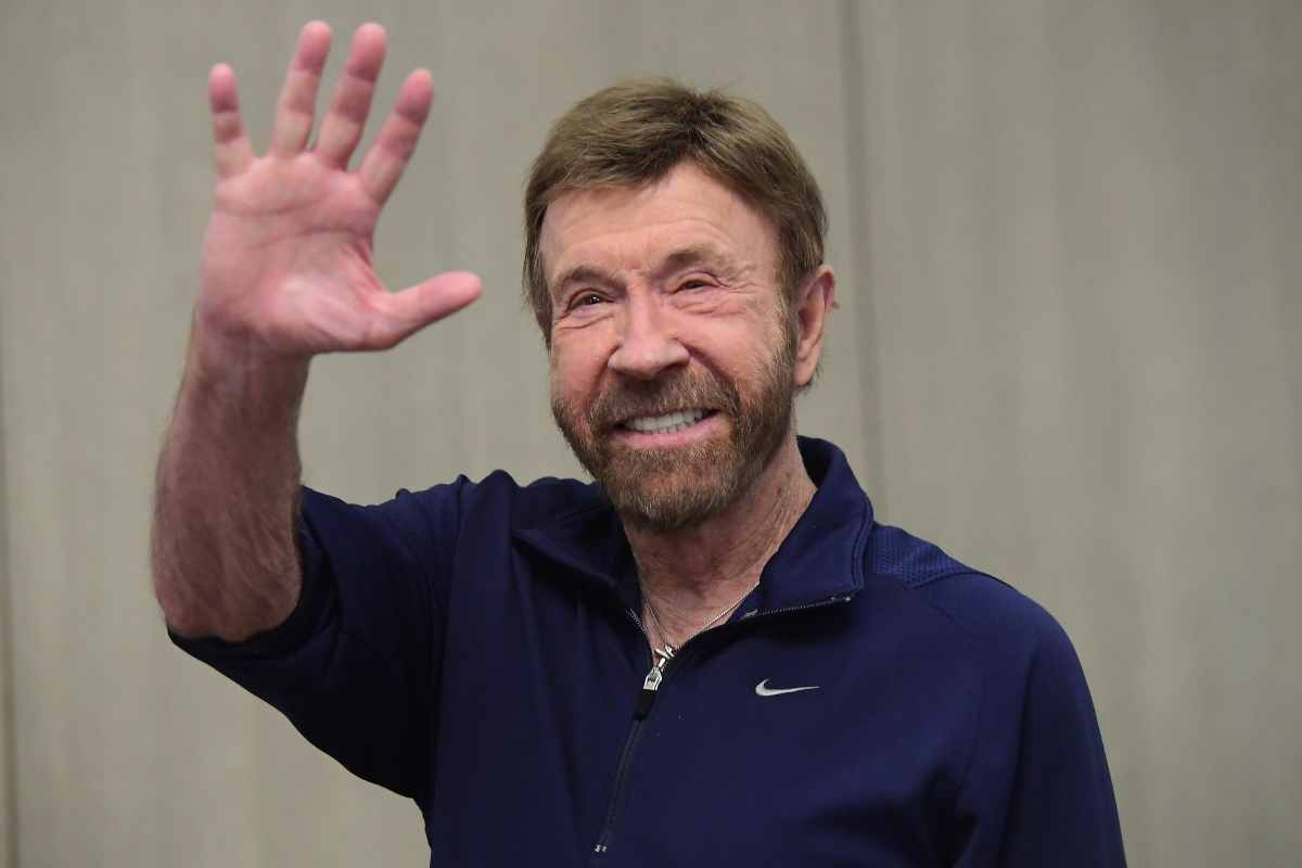 Chuck Norris con t-shirt blu saluta verso l'obiettivo.